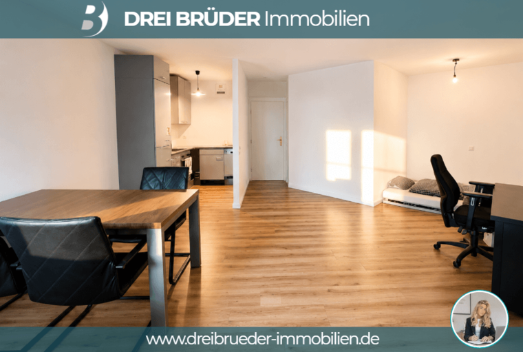 Ein helles, modernes Zimmer mit Holzfußboden. Auf der linken Seite befindet sich eine Küchenzeile mit Schränken und einem Esstisch. Rechts steht ein Schreibtisch mit einem Stuhl. An der Wand ist ein Licht angebracht, und Sonnenschein fällt durch ein Fenster.
