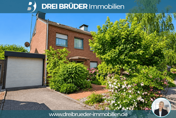 Ein zweigeschossiges, rotes Wohnhaus mit grünen Büschen und Blumen im Vordergrund. Links befindet sich eine Garage mit einem Rolltor. Der Garten ist gepflegt und bietet eine einladende Atmosphäre.