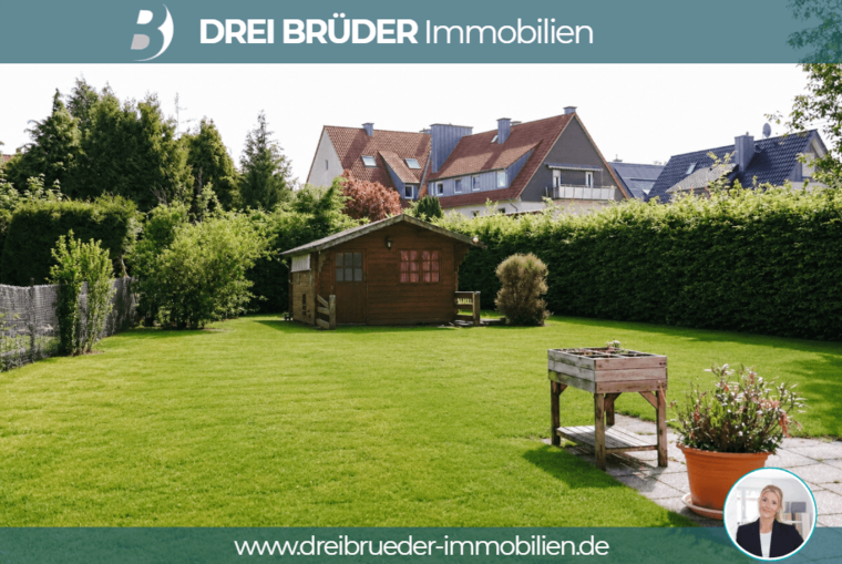 Ein grüner Garten mit einem kleinen Holzhaus und einem Tisch aus Holz ist zu sehen. Im Hintergrund sind Bäume und Wohnhäuser zu erkennen. Der Garten wirkt gepflegt und einladend.