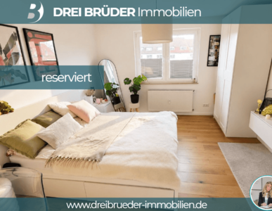 Ein modernes Schlafzimmer mit einem großen Bett, dekorativen Kissen und einer gemütlichen Decke. An der Wand hängen Bilder. Neben dem Bett steht ein kleiner Tisch mit Pflanzen. Es gibt ein Fenster, durch das Tageslicht strömt. Der Raum wirkt hell und einladend.