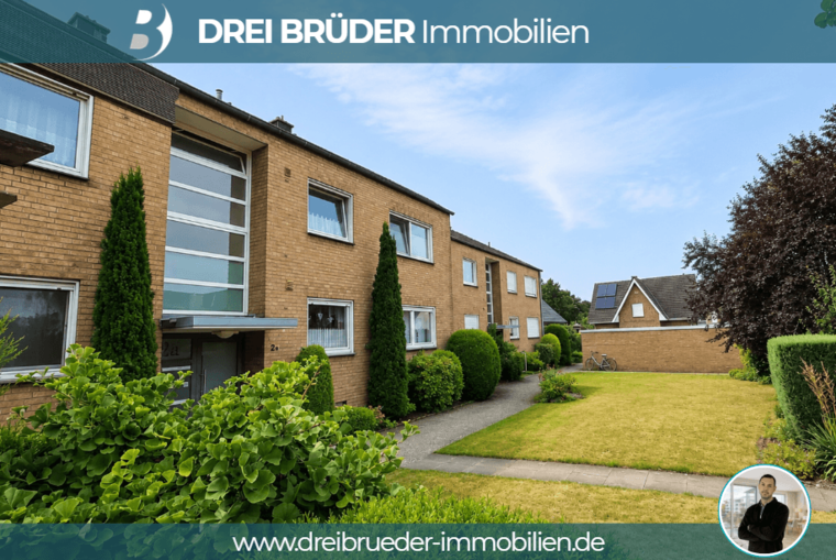 Ein zweigeschossiges Wohngebäude aus Ziegelstein mit großen Fenstern. Vor dem Gebäude befindet sich ein gepflegter Garten mit Grünanlagen und einem schmalen Weg. Im Hintergrund sind weitere Gebäude sichtbar. Oben links ist das Logo "Drei Brüder Immobilien" zu sehen.